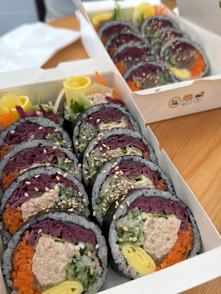 Two boxes of sliced kimbap rolls with sesame seeds
